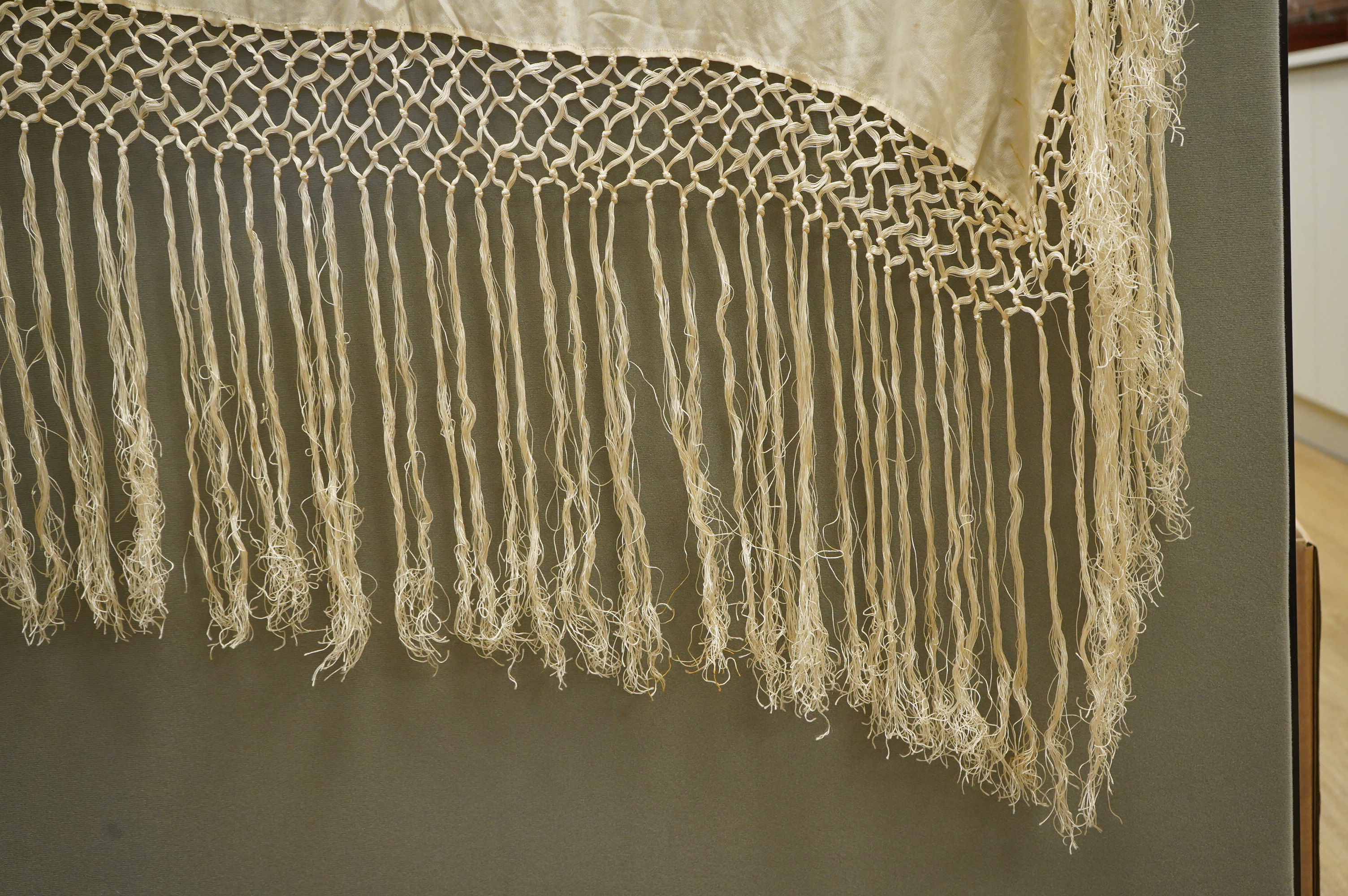 A unusual Chinese 1920’s-30’s cream silk fringed shawl, embroidered with a large central motif of a phoenix in flight, embroidered in bright multi coloured silks. 108cm x 100cm, Condition - there are some stains.